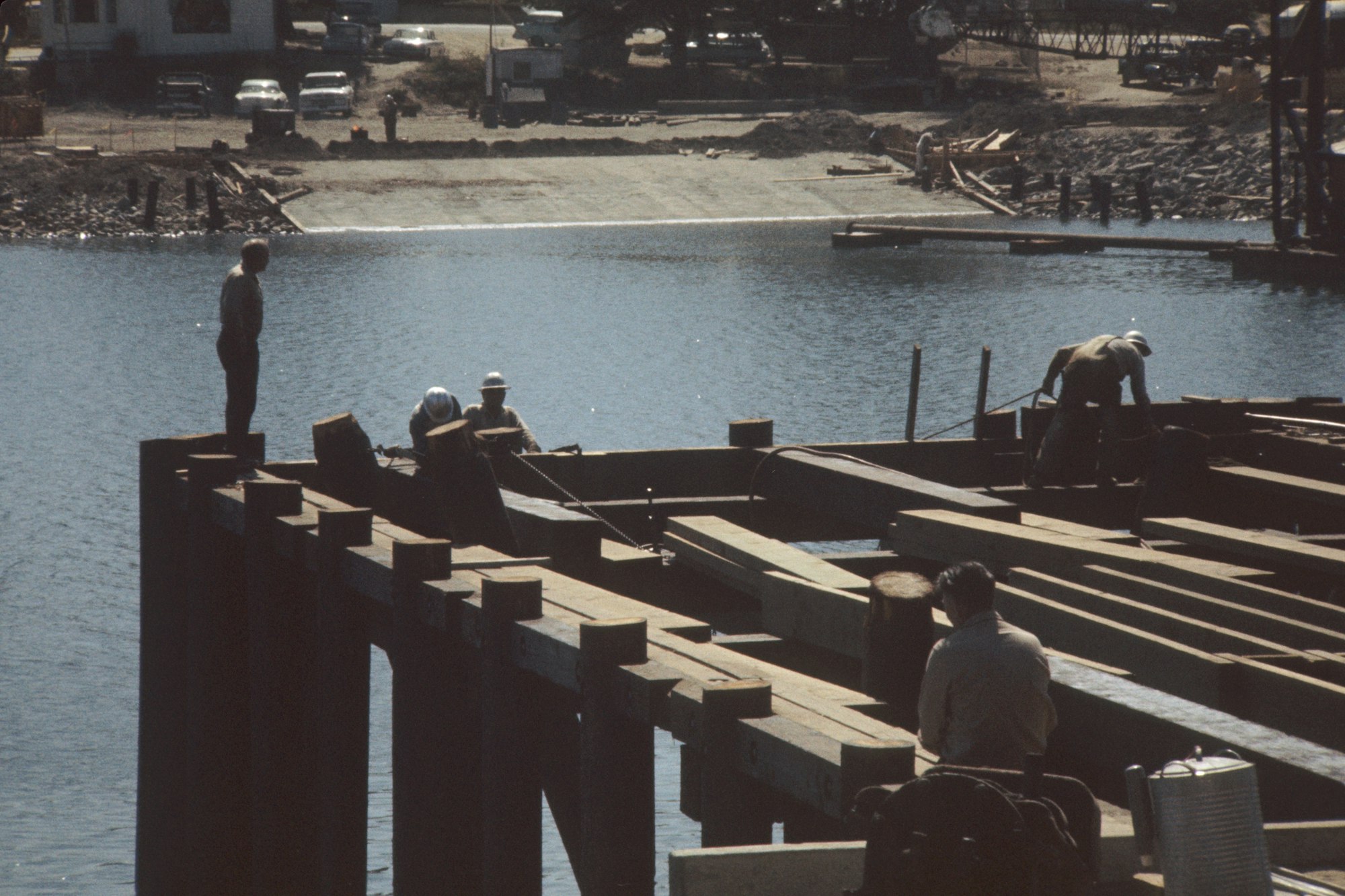 Workers on a construction site near water, possibly building a dock or bridge.