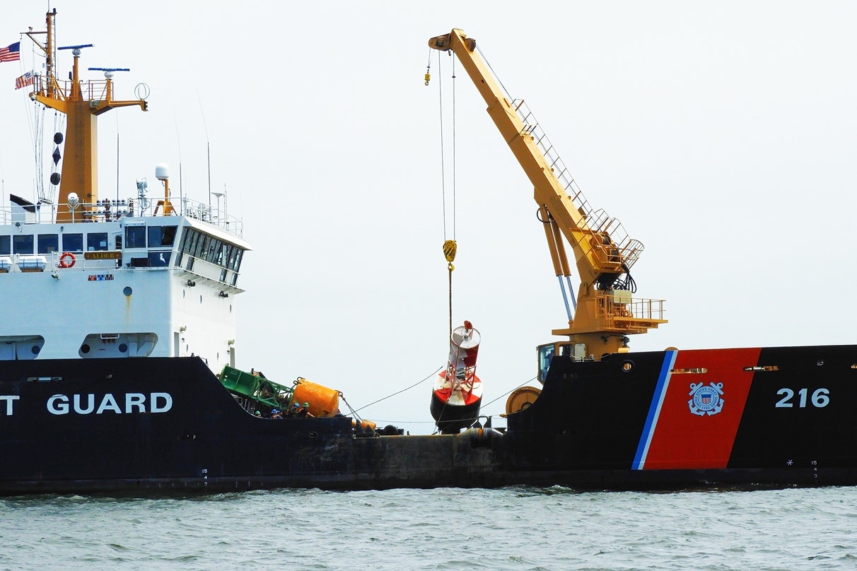 A crane lifting a buoy near a ship with "COAST GUARD" text.