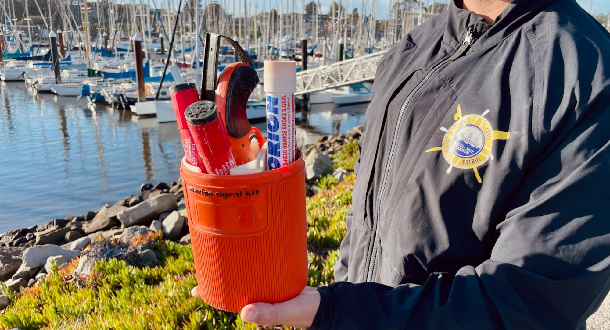 Person holding a marine signal kit with boats and a marina in the background.