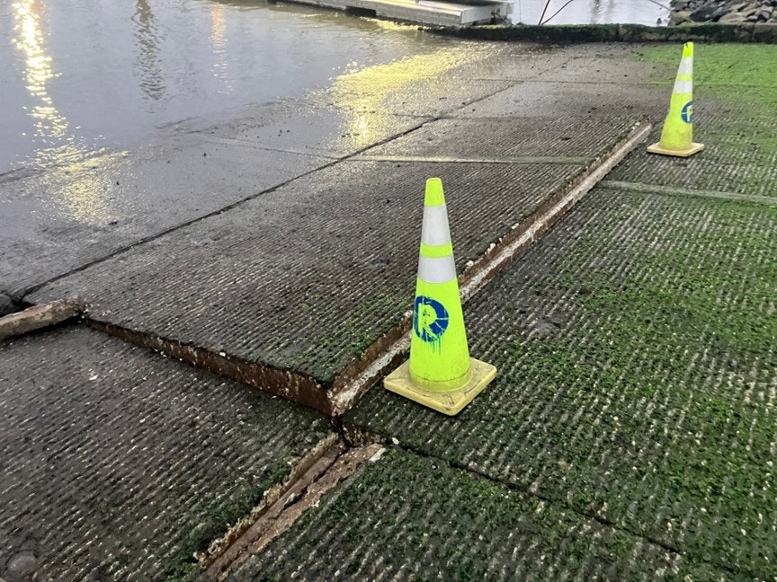 Two traffic cones mark a raised edge on a wet, concrete ramp by the water.