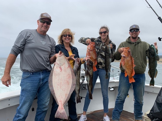 Four people on a boat holding up various fish they caught, with the ocean in the background.