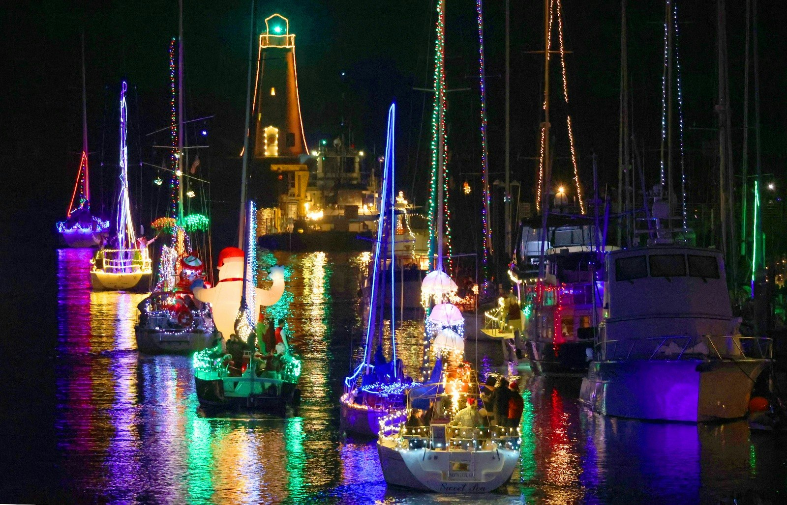 Boats decorated with colorful lights and holiday decorations at night on the water.