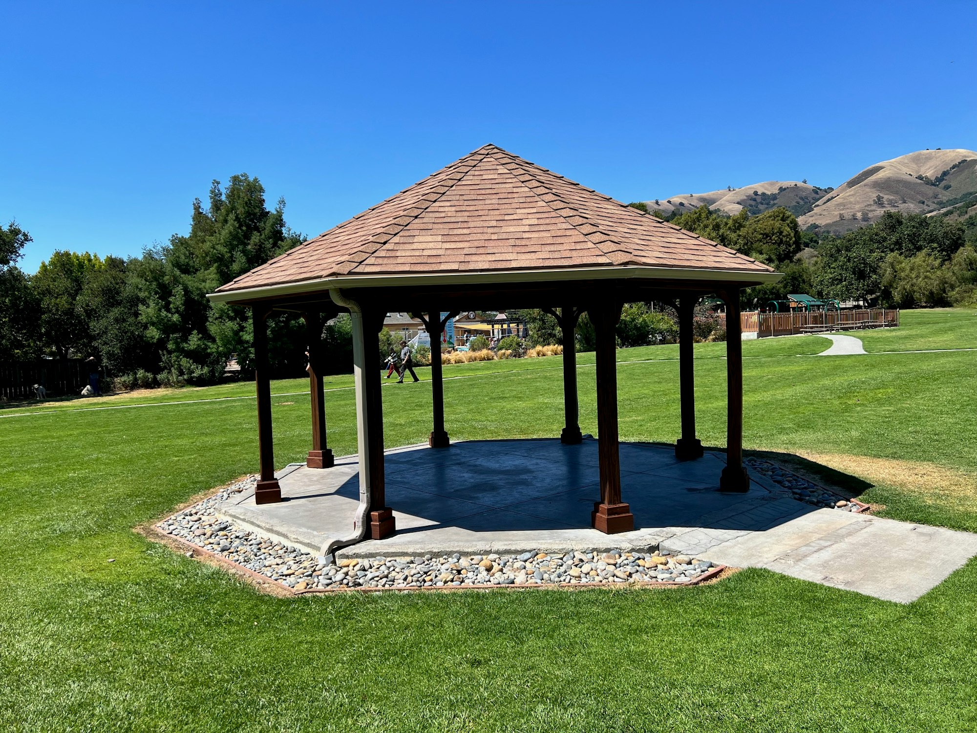 A gazebo in a grassy park with trees and hills in the background on a sunny day.