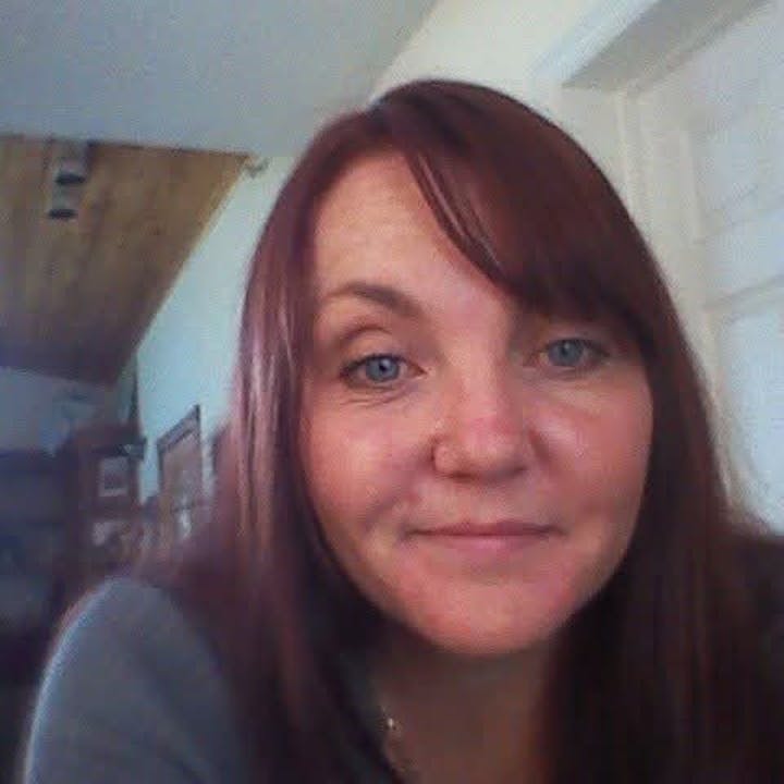 A person with long, brown hair indoors, smiling slightly at the camera.