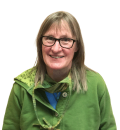 A smiling person with glasses wearing a green jacket and blue shirt.