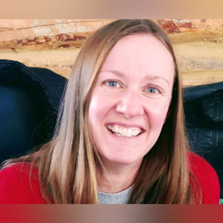 A smiling woman in a red top with a blurred background.