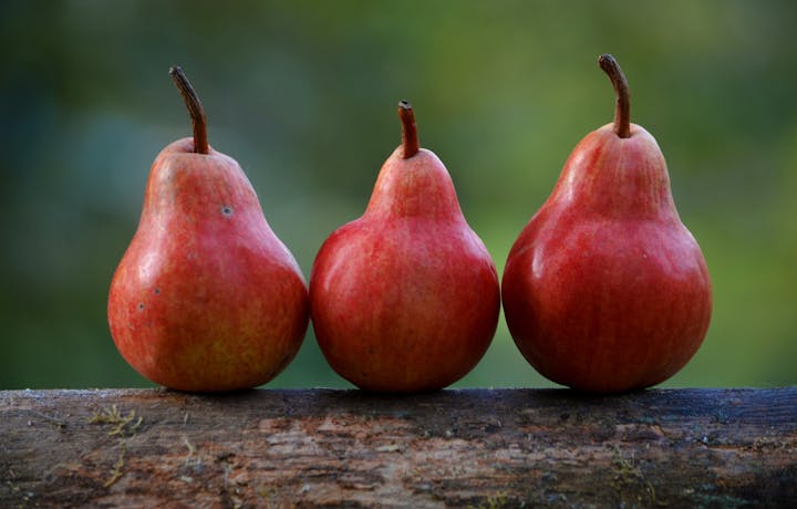 Three red pears lined up on a wooden surface with a blurred green background.