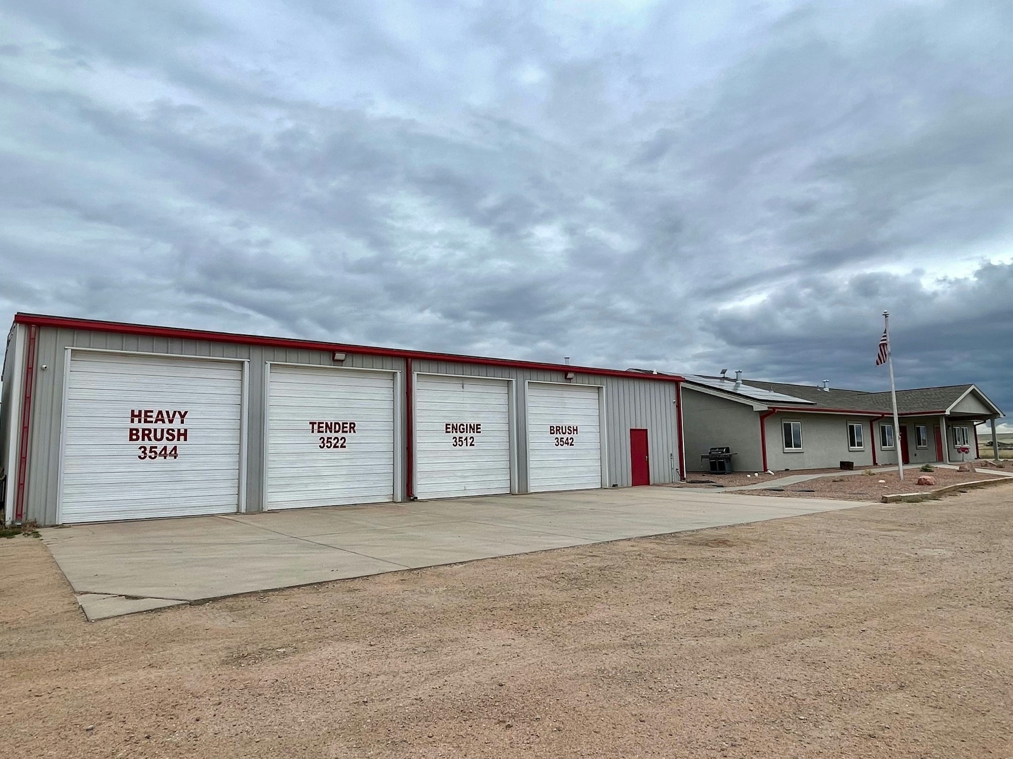 A fire station with labeled garage doors for different firefighting vehicles under a cloudy sky.