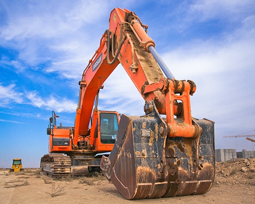 An orange excavator on a construction site under a blue sky.