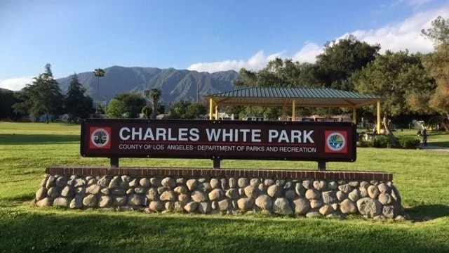 The image shows a sign for Charles White Park in Los Angeles, featuring a stone base and a scenic park backdrop.