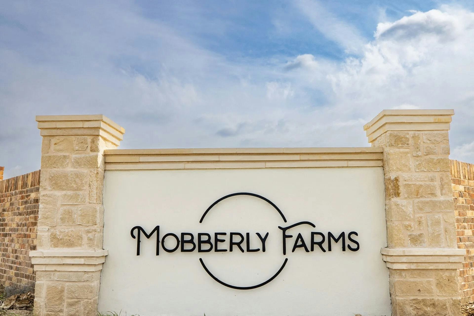 Stone entrance sign for "Mobberly Farms" under a partly cloudy sky.