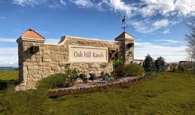 Sign for "Oak Hill Ranch" on a stone structure with landscaping, under a partly cloudy sky.