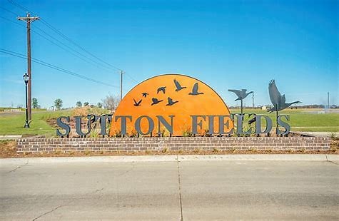 A sign reading "Sutton Fields" with bird silhouettes against an orange circle, set in a grassy area.