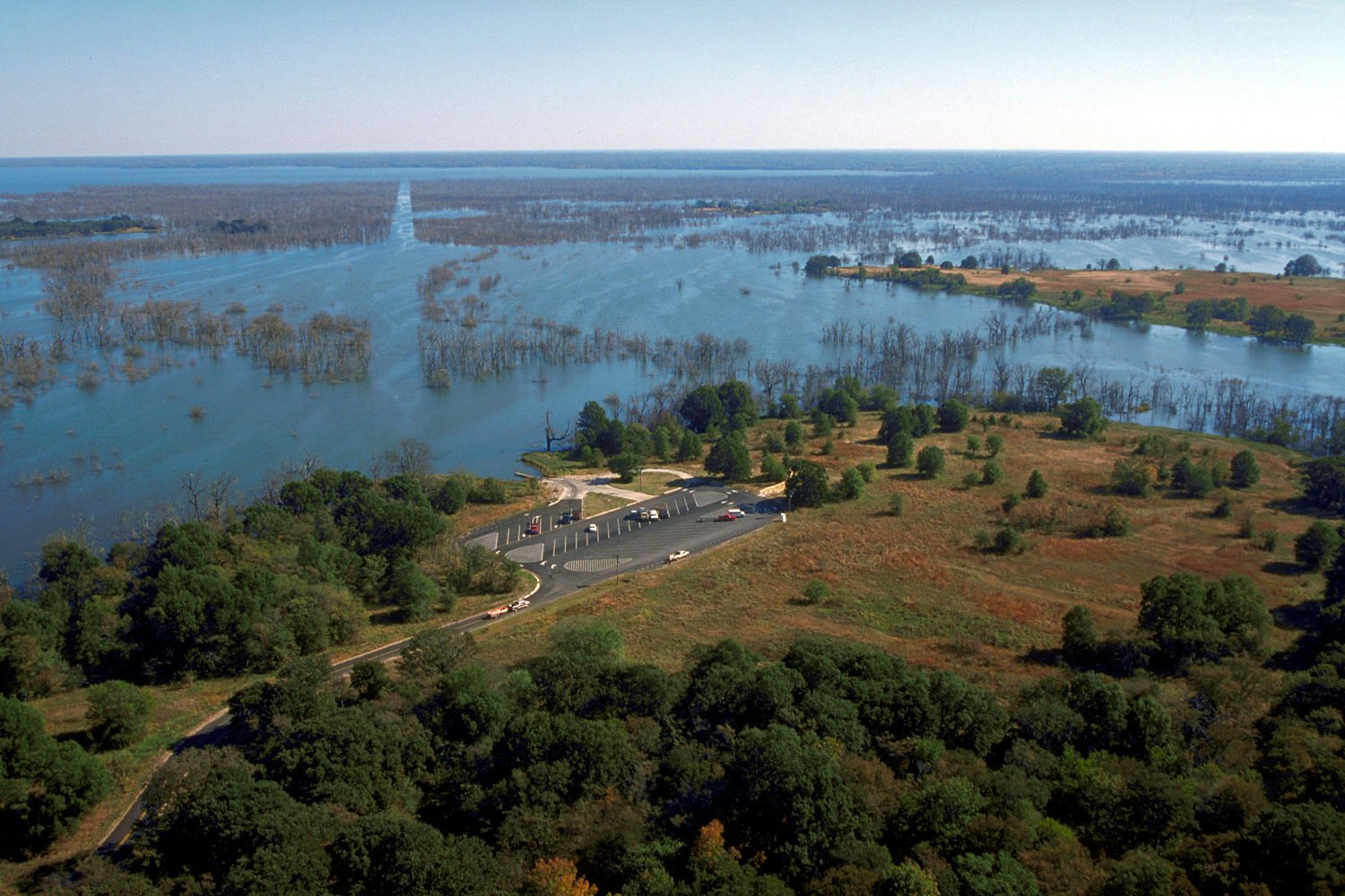 An aerial view of a flooded landscape with sparse trees and a parking area near the water's edge, showcasing nature's beauty.