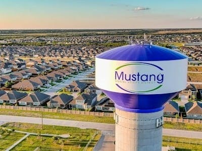 Water tower labeled "Mustang Special Utility District" overlooking a residential area with houses and roads.