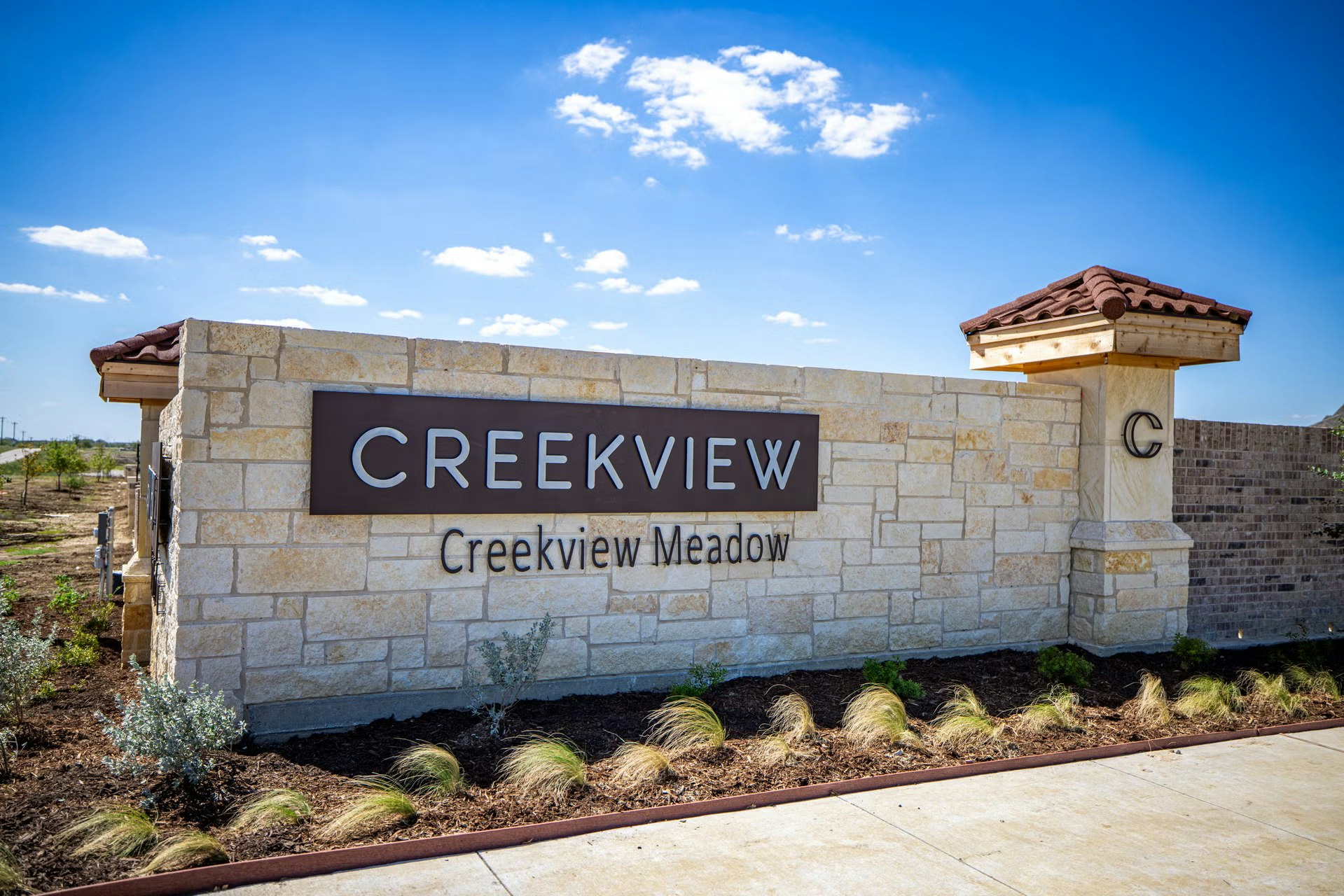 Stone entrance sign for "Creekview Creekview Meadow" with landscaping and a clear sky background.