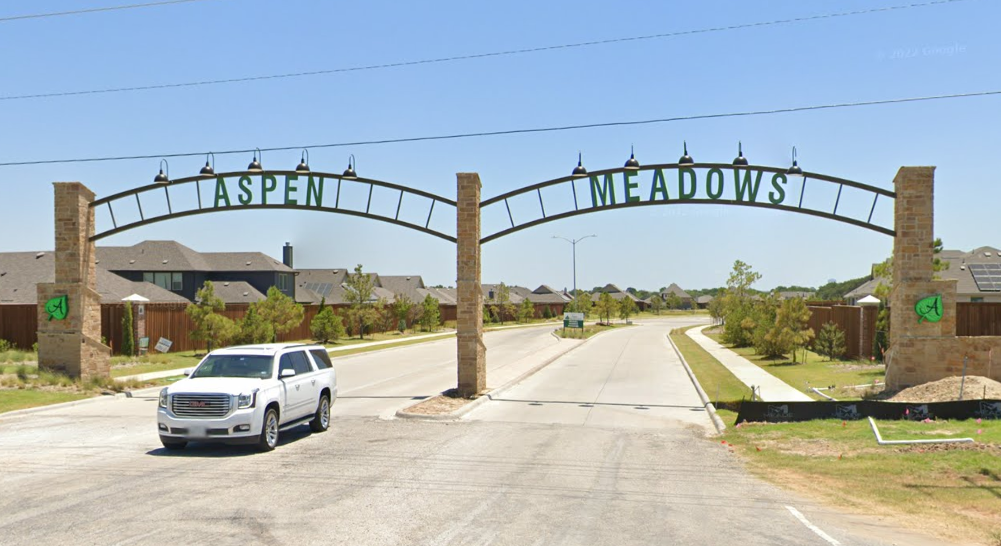 A vehicle passes under the "Aspen Meadows" archway entrance to a residential neighborhood.