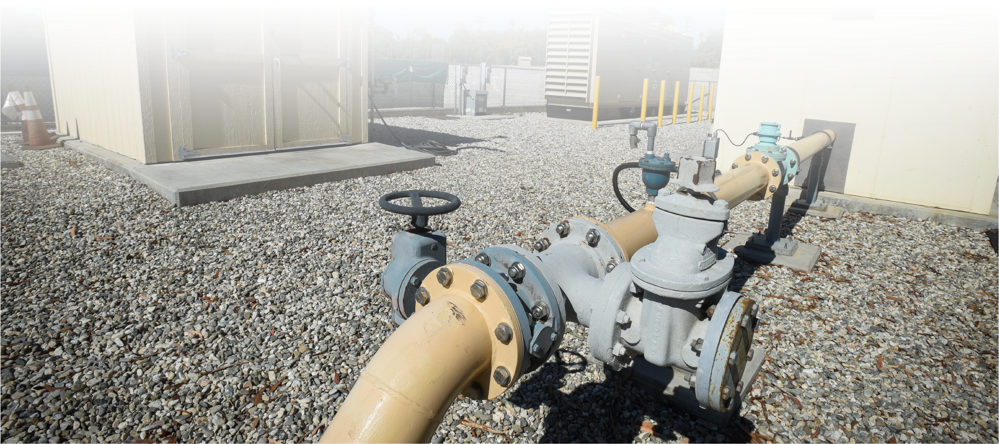 The image features industrial piping, valves, and a facility surrounded by gravel and utility structures.