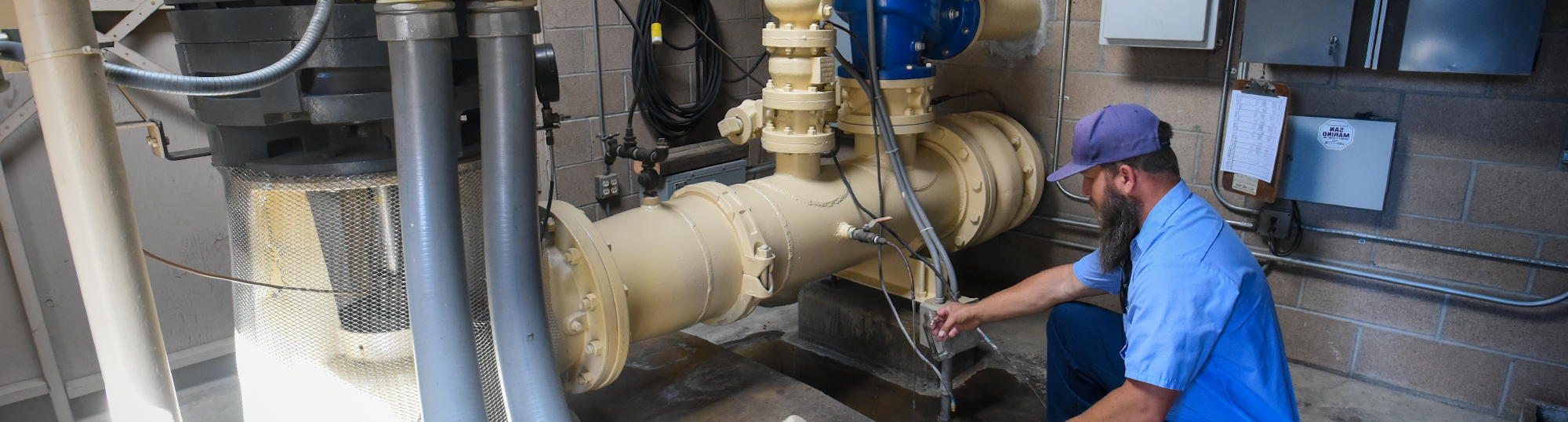 A worker inspects a large valve and pipes in a facility, ensuring proper functioning of the water system.