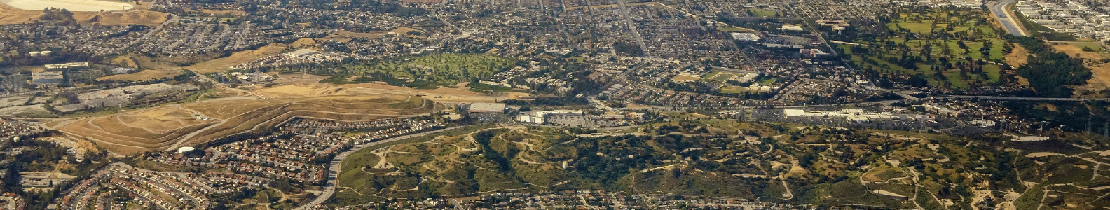 An aerial view of a suburban area with hills, residential neighborhoods, parks, and commercial buildings.
