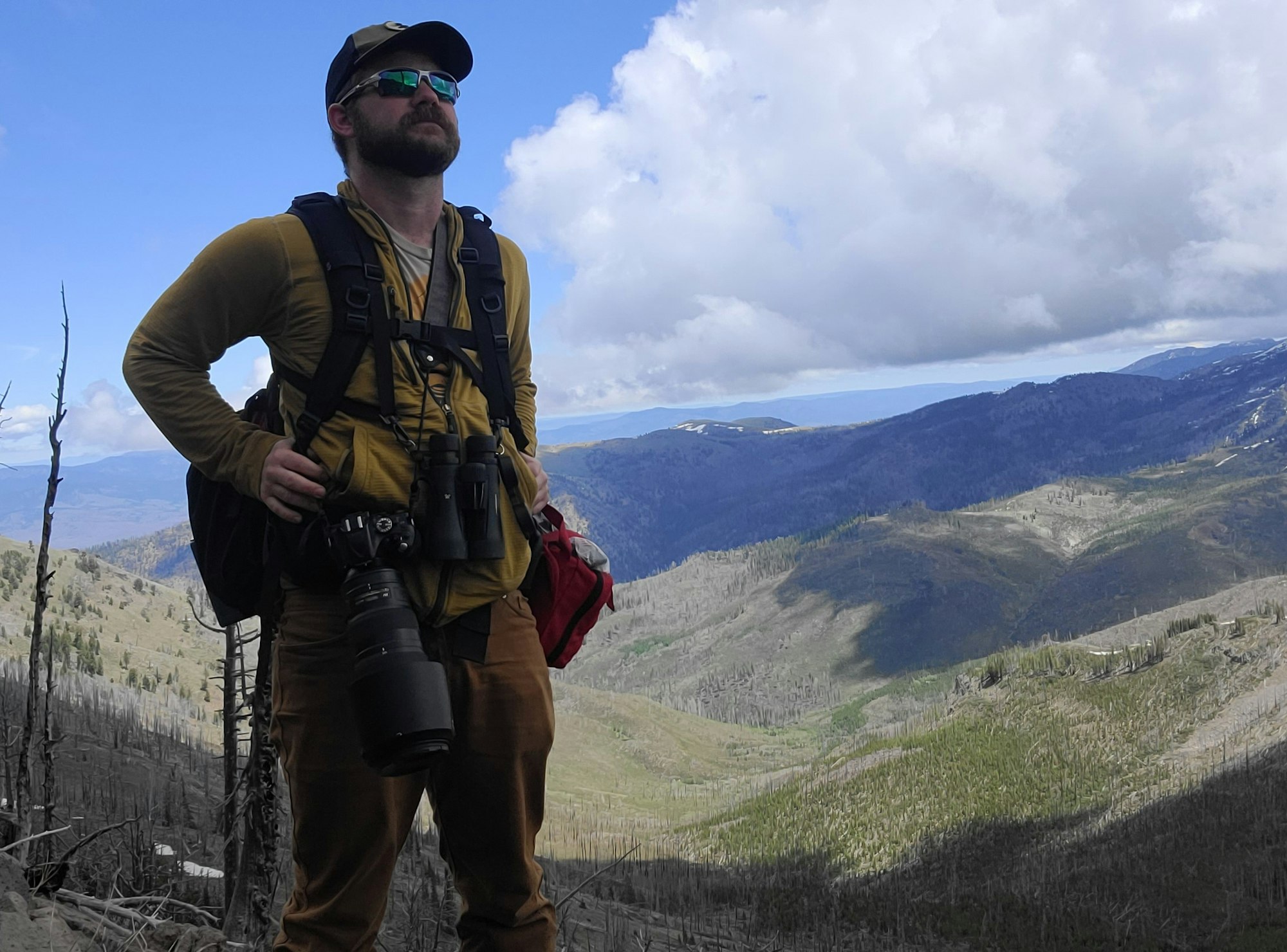 Man standing with cameras, mountains in background