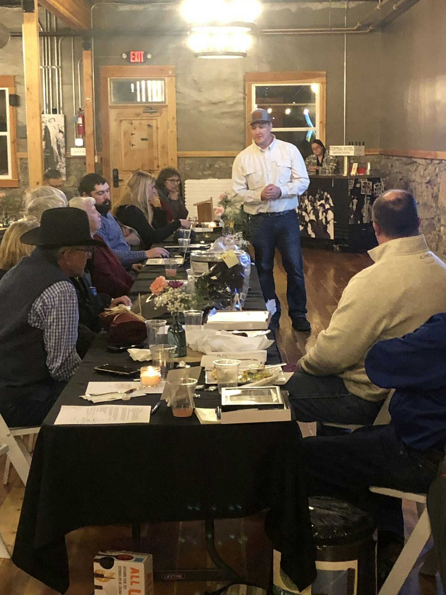 A person addressing a group at a dimly lit event with tables, candles, and attentive listeners.