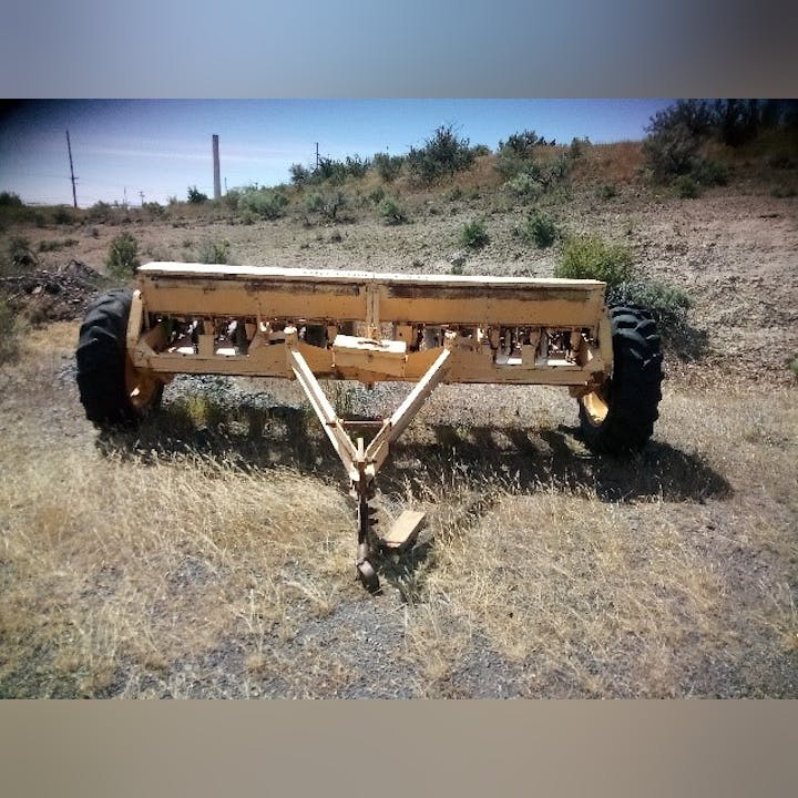 An old farm trailer with missing front wheels abandoned in a dry field.