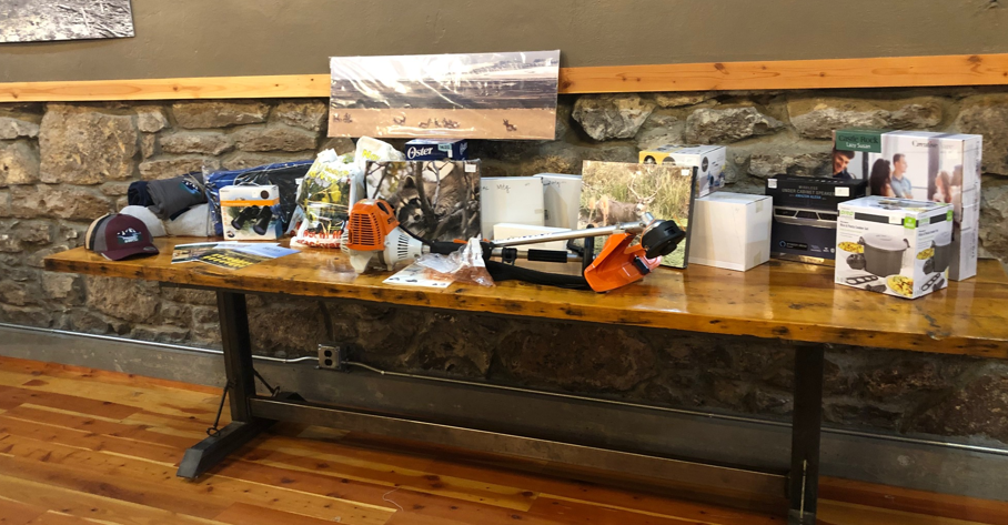 A table with various items, possibly for a raffle or auction, including outdoor gear, electronics, and household products.