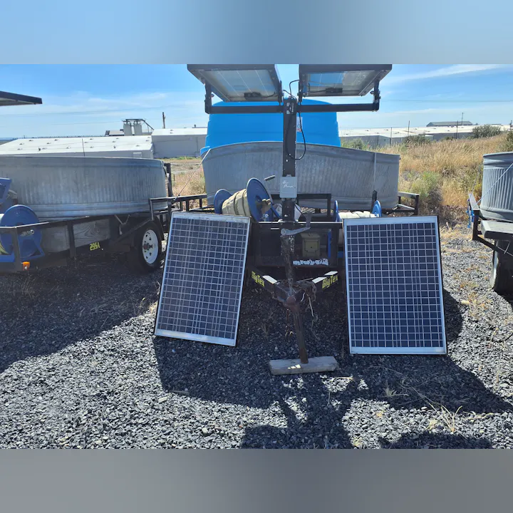 The image shows a trailer with solar panels, water tanks, and equipment on rocky terrain under a clear blue sky.