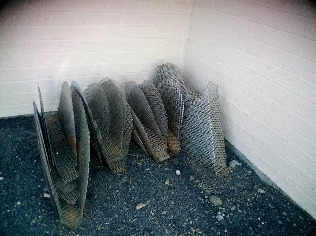 Rolled up metal fencing stacked outside against a white wall.