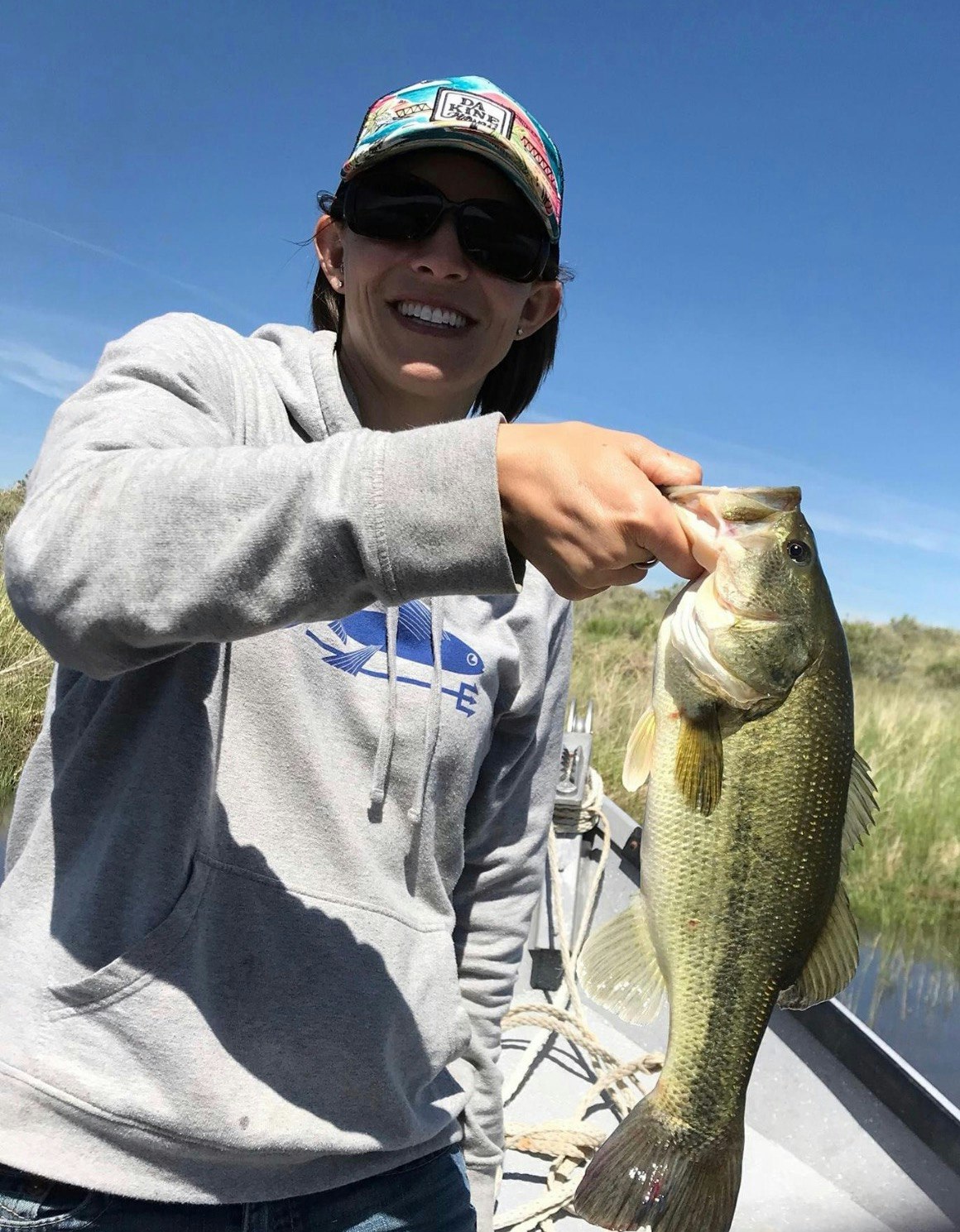 A person holding a fish on a boat, both in sunlight with a clear sky.