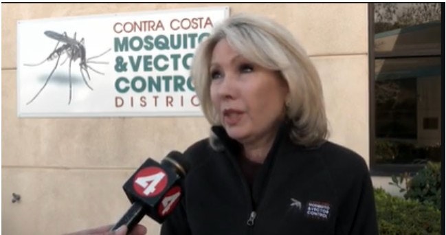 A woman speaking into a microphone outside the Contra Costa Mosquito & Vector Control District building.