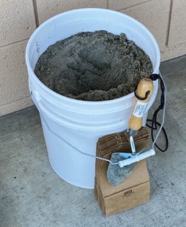 A bucket filled with sand, a trowel, and small paper bags.