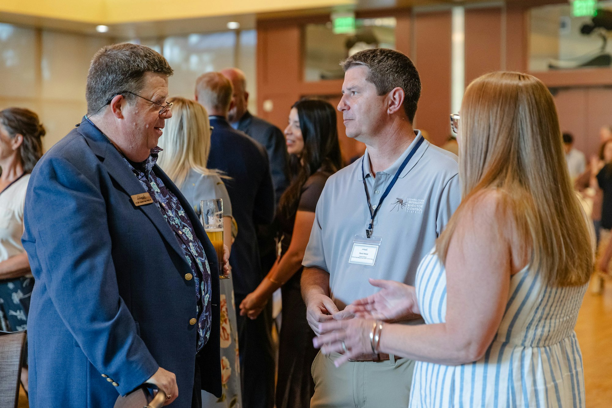 People are conversing at a social or networking event, some wearing name tags and holding drinks.