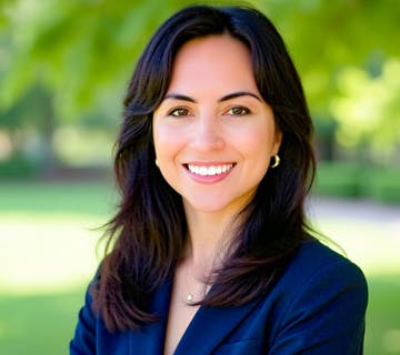 The image shows a smiling woman in a blazer with long dark hair, standing outdoors against a green backdrop.
