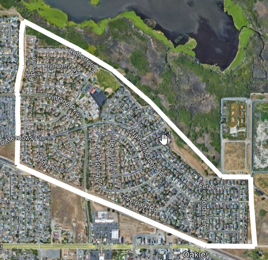 Satellite view of a suburban area with streets, houses, and greenery next to a body of water.