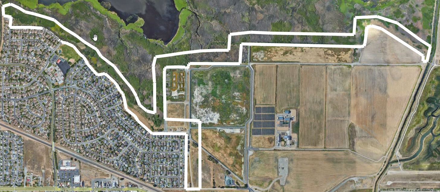 Aerial view of a residential area alongside agricultural fields and what appears to be a water treatment facility.