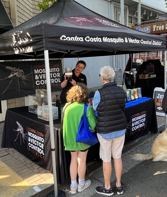 Information booth about mosquito control with staff explaining products to visitors.
