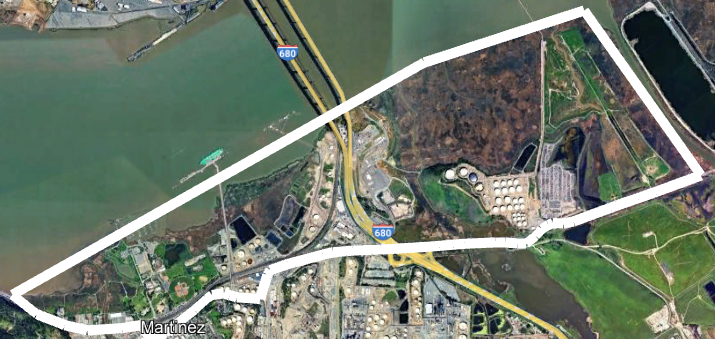 Aerial view of a landscape with highways, a bridge, industrial areas, and a large outlined section near a water body.