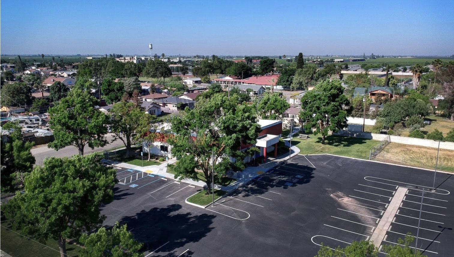 Aerial view of a parking lot, buildings, and greenery in a suburban area.