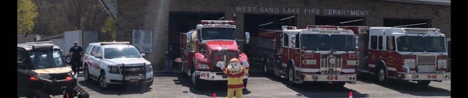 Fire trucks and a mascot in front of West Sand Lake Fire Department.