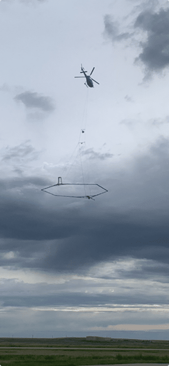 Helicopter carrying a large, hexagonal frame hanging below it in a cloudy sky.
