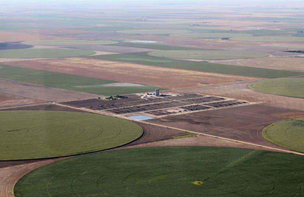 Aerial view of agricultural fields with circular and rectangular patterns, and a central facility with buildings and fenced areas.
