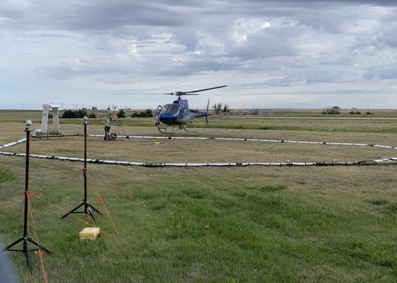 A helicopter landing on a grassy field with a man nearby and equipment in view.