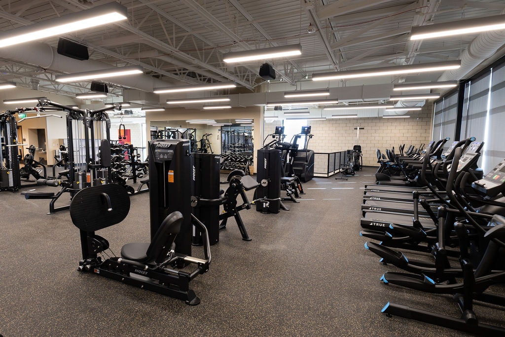 A modern gym filled with various workout machines and cardio equipment in a spacious, well-lit environment.