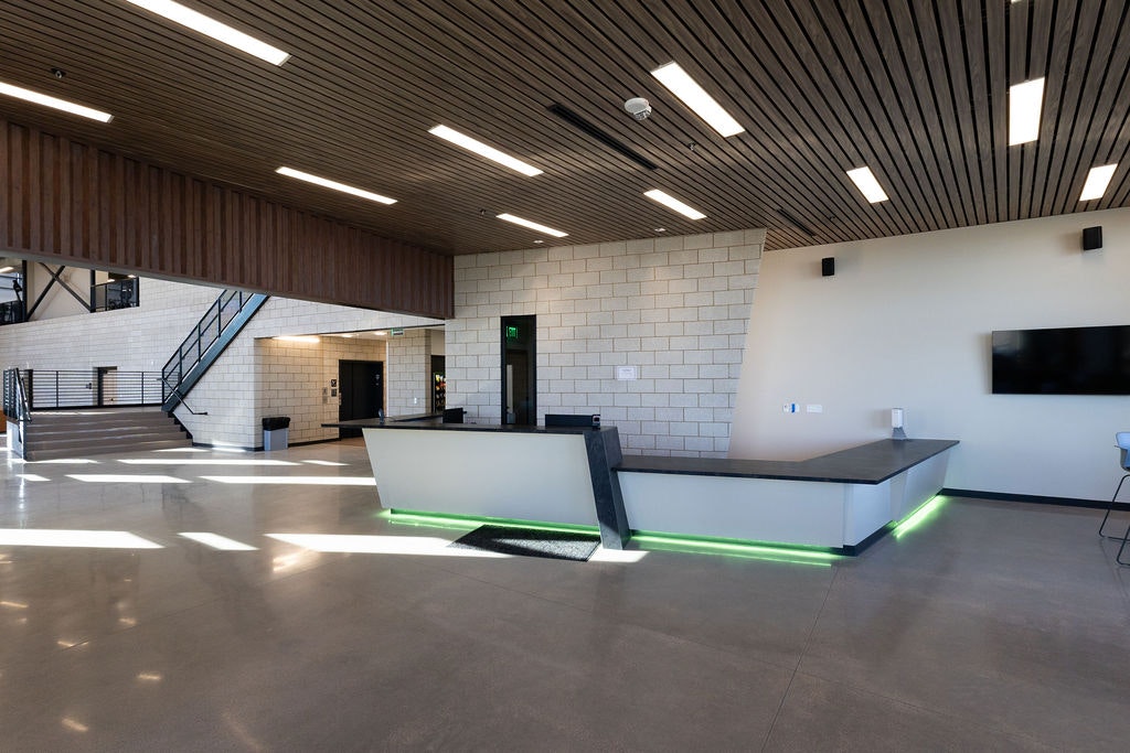 A modern, spacious reception area with wooden ceilings, minimalist design, and a sleek front desk featuring green lighting.