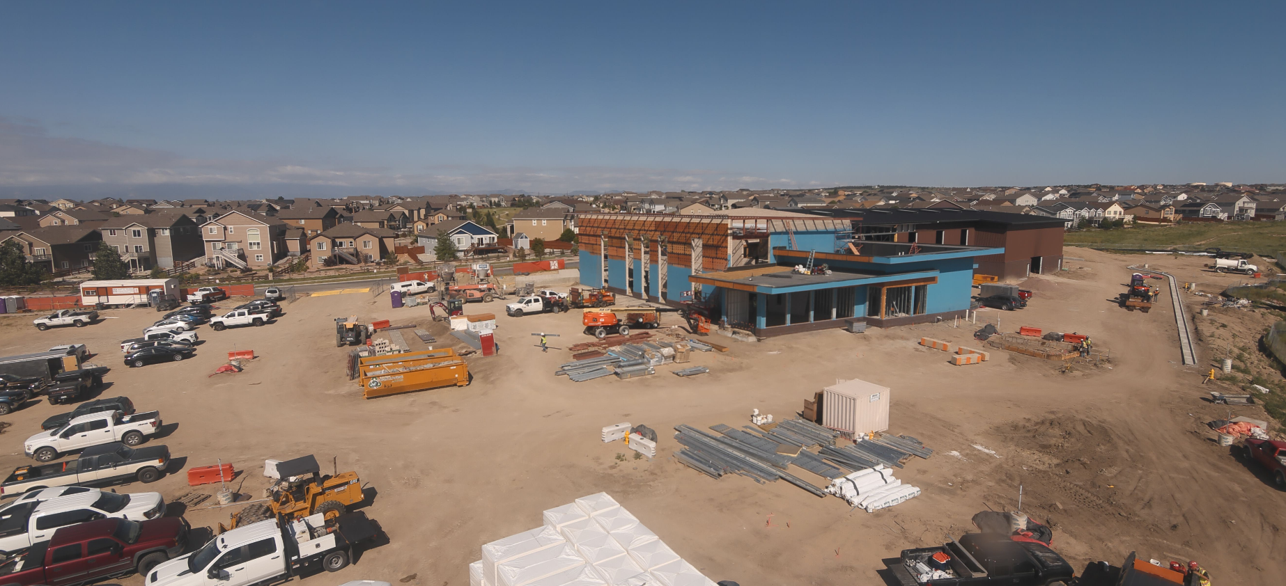 A construction site with vehicles, materials, and a partially built structure, set in a suburban neighborhood.