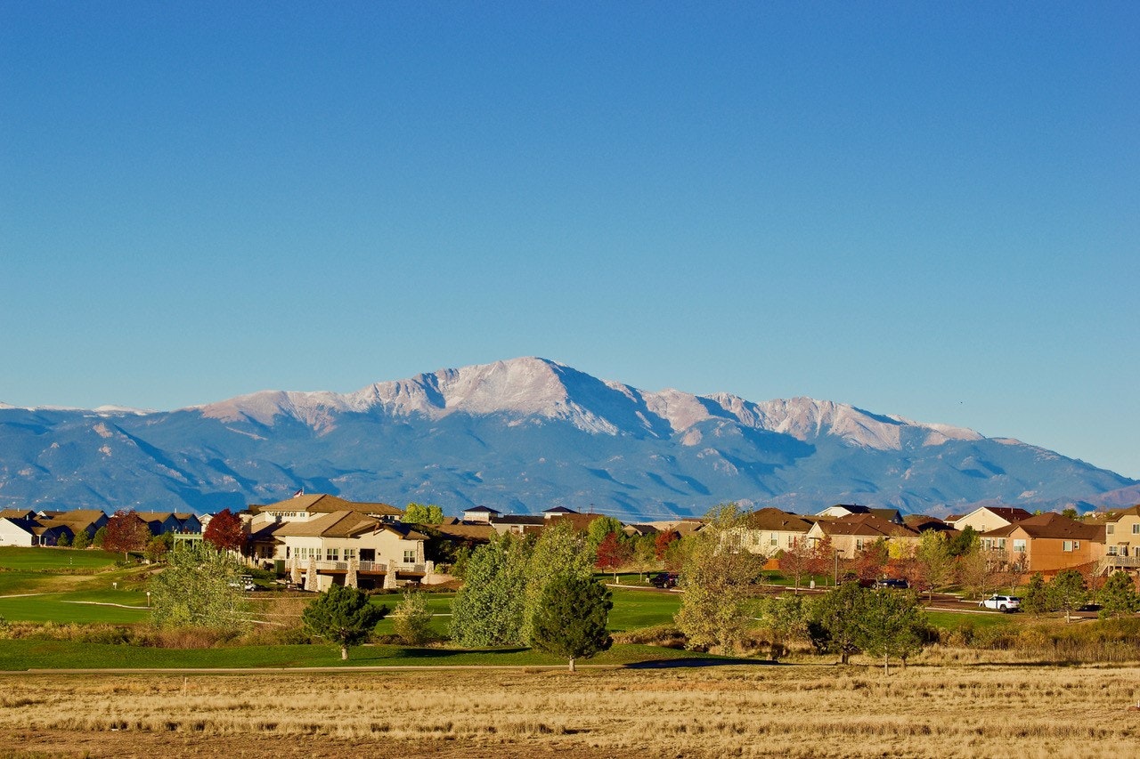 A scenic view featuring houses in the foreground and a majestic snow-capped mountain range under a clear blue sky.