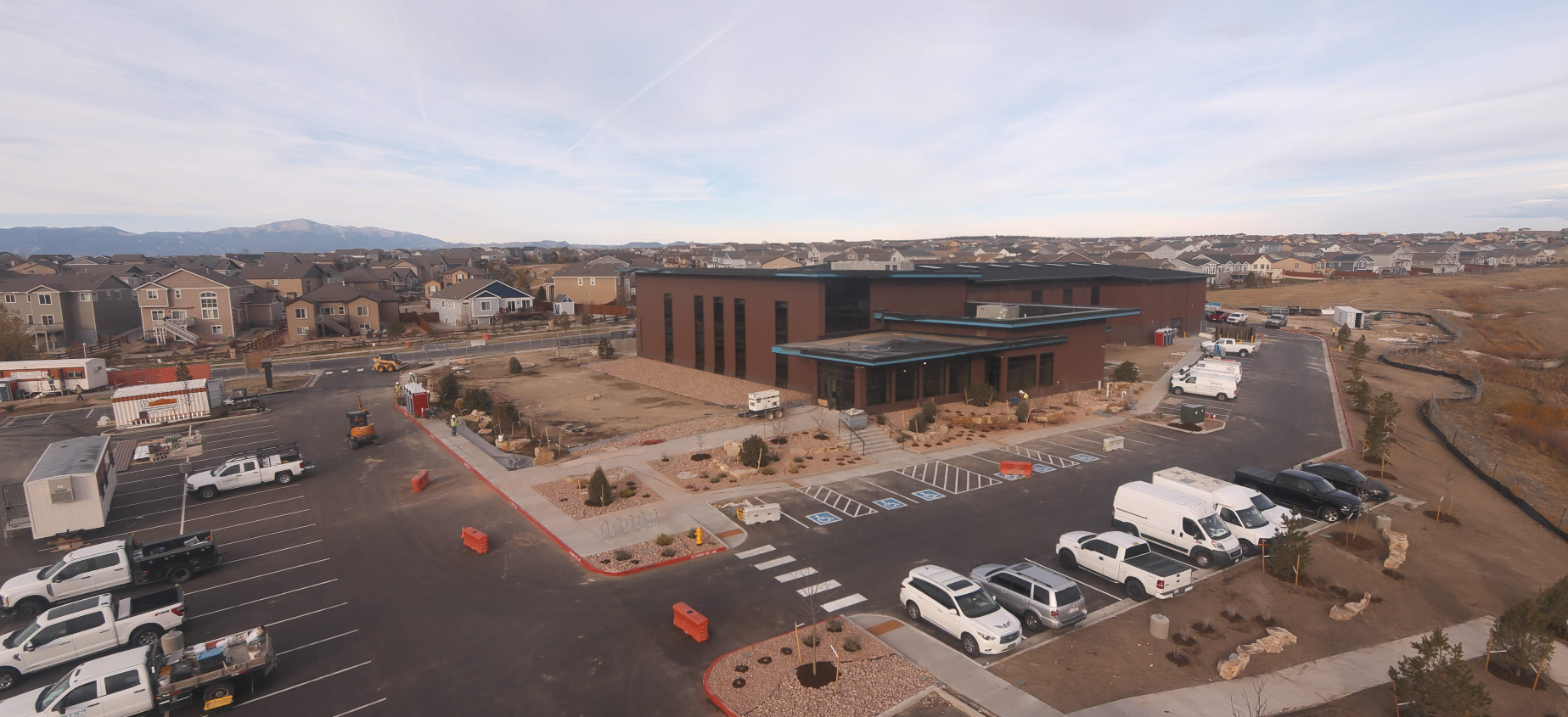 A large brown building with parked vehicles, surrounded by residential homes and construction equipment in a suburban area.
