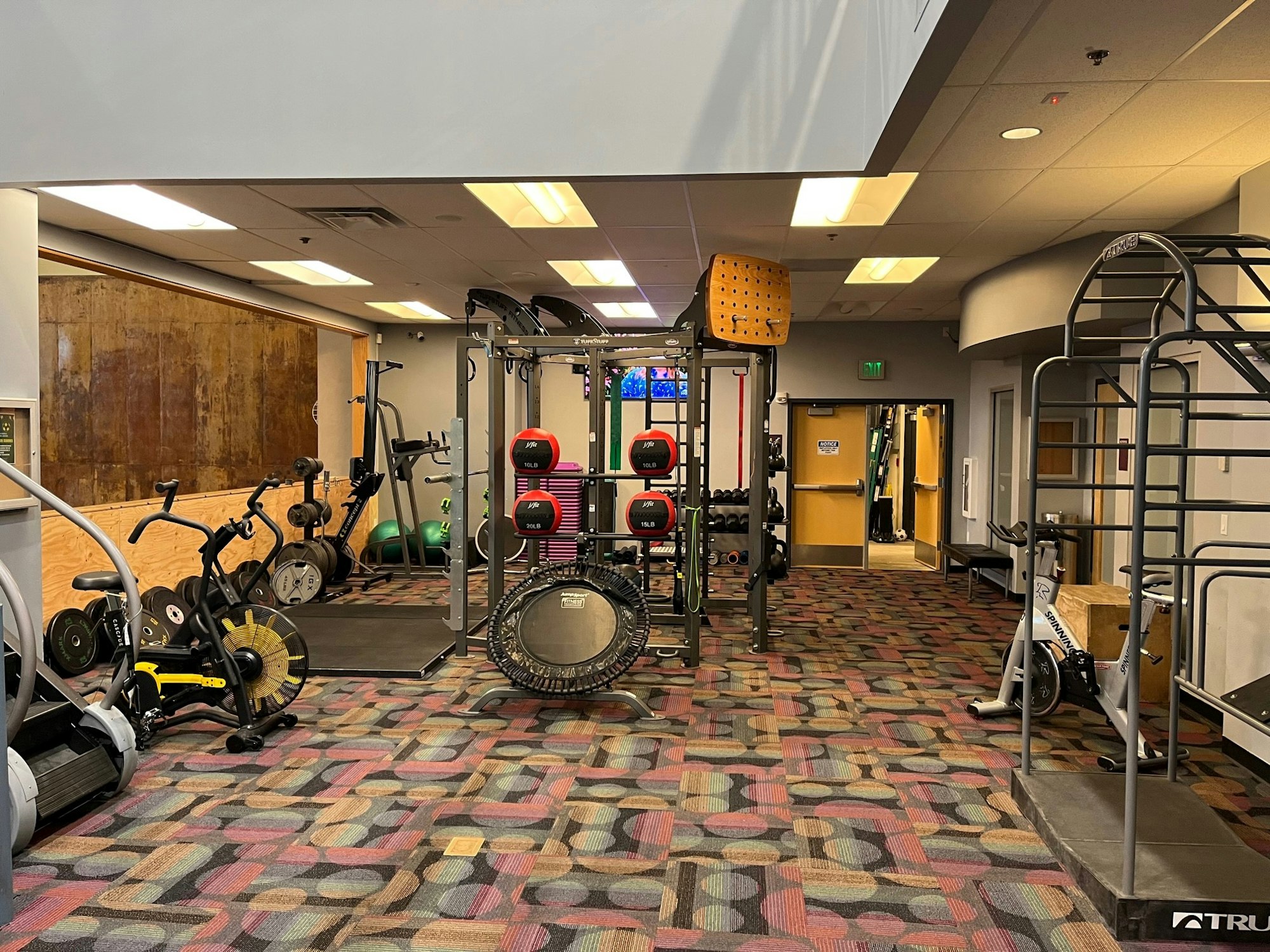 A gym area featuring various exercise equipment, weights, and workout stations, set in a brightly lit space.